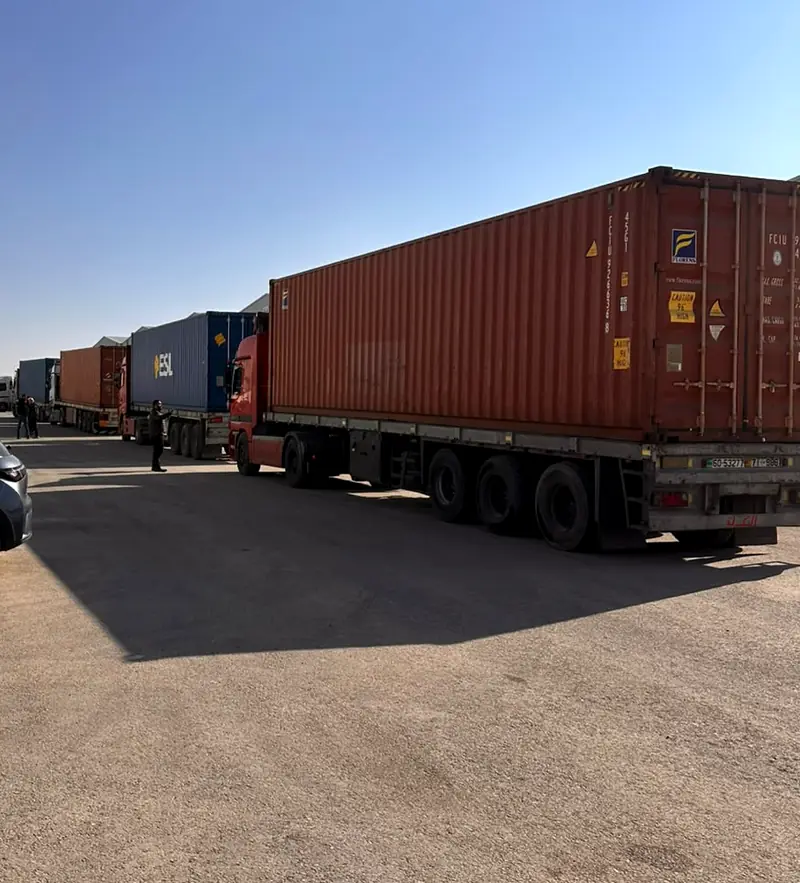 A line of container trucks with Jordanian plates arriving at a warehouse complex in Jordan